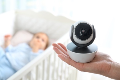 Photo of Woman holding baby camera near crib with child in room. Video nanny