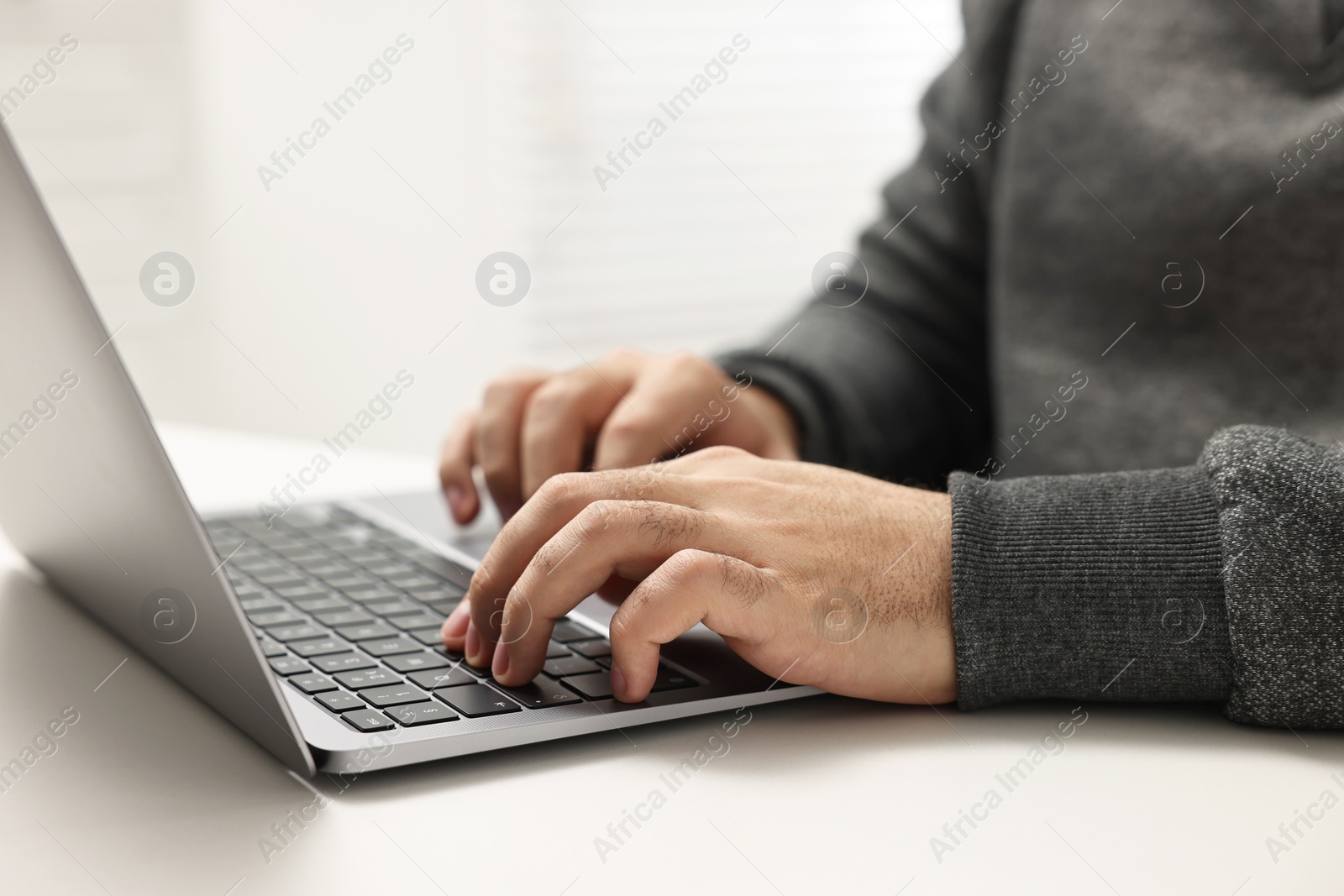 Photo of E-learning. Young man using laptop at white table, closeup