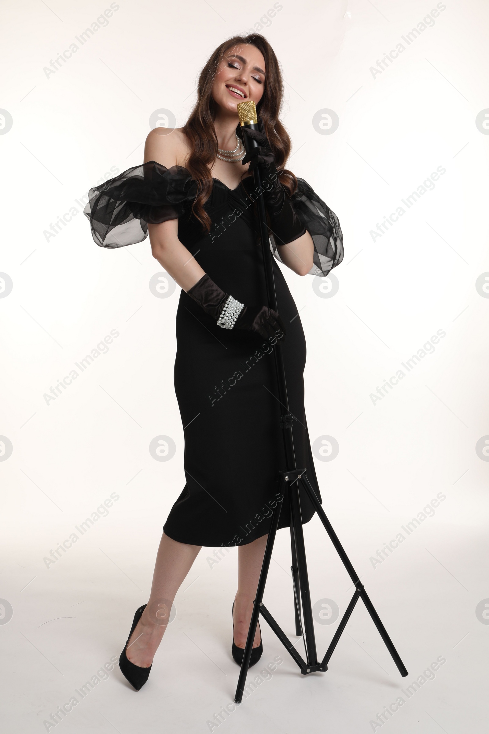 Photo of Beautiful young woman in stylish dress with microphone singing on white background