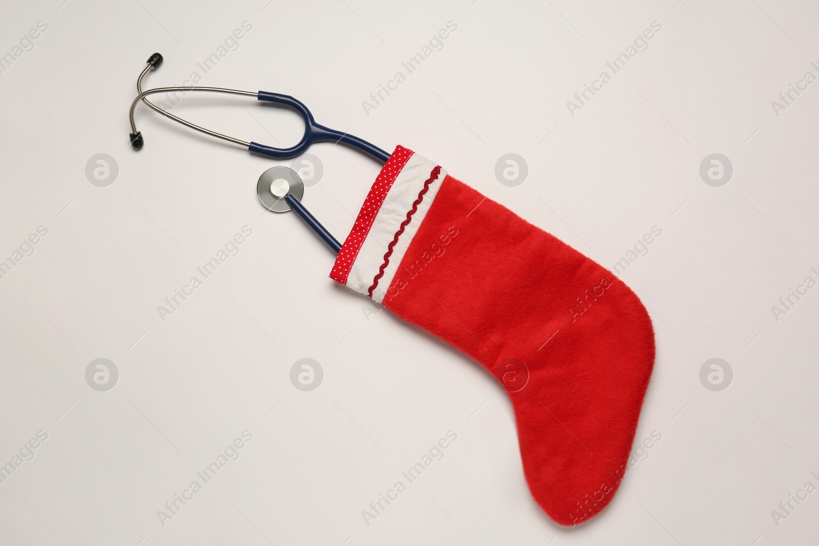 Photo of Greeting card for doctor with stethoscope and Christmas stocking on white background, top view