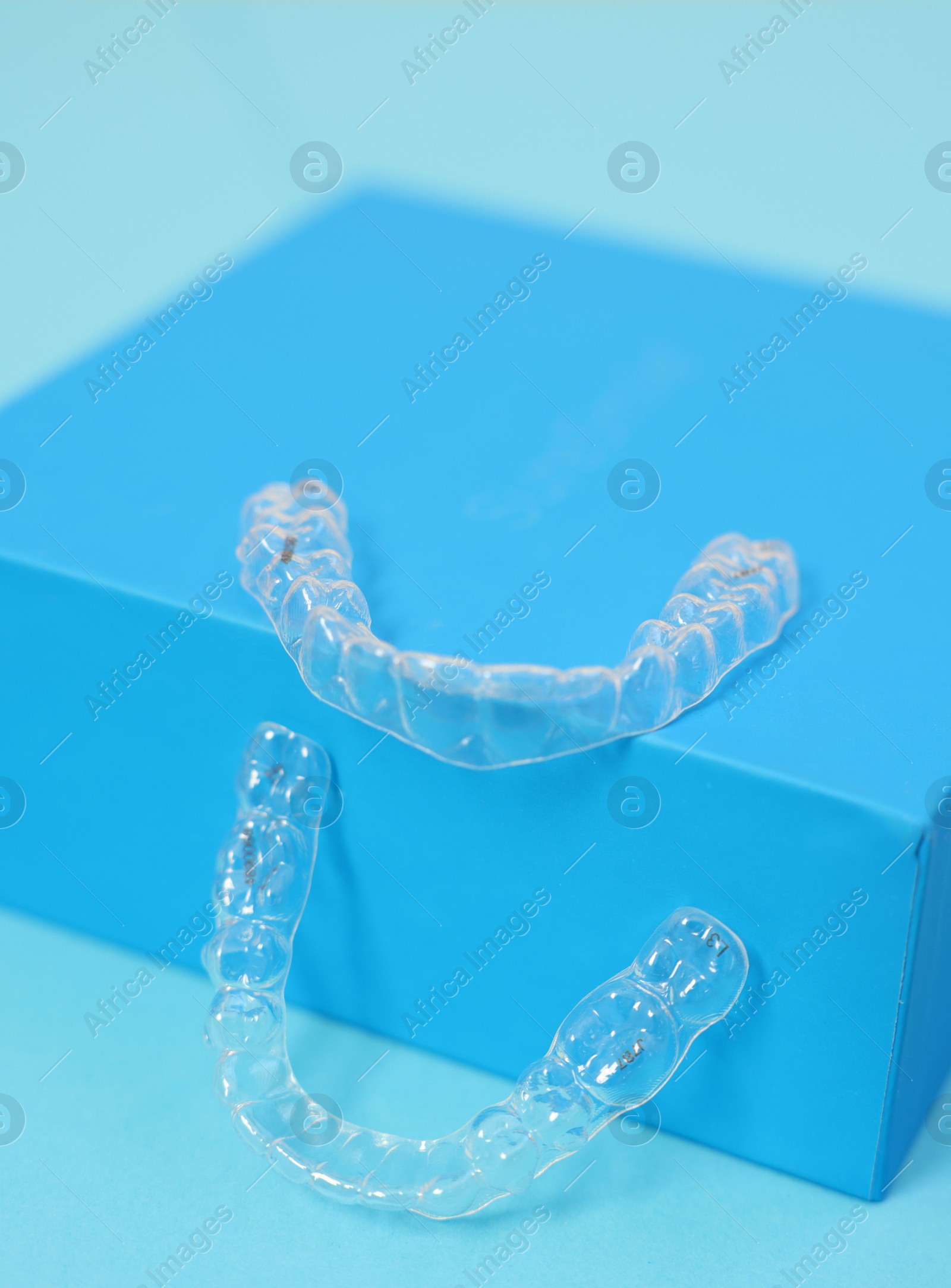 Photo of Transparent dental aligners on light blue background, closeup