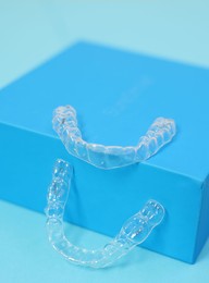 Photo of Transparent dental aligners on light blue background, closeup