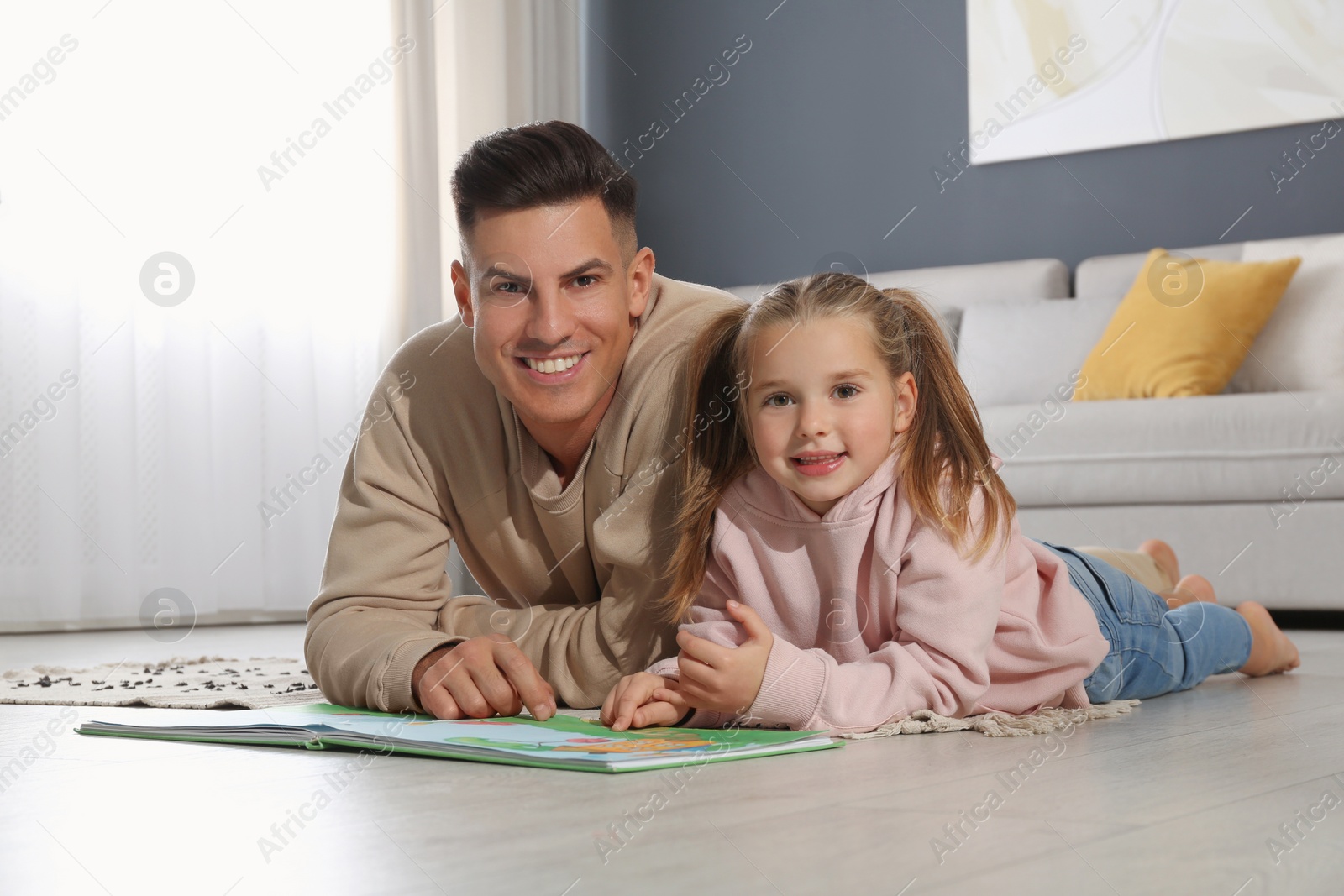 Photo of Father and his daughter reading book at home. Floor heating concept