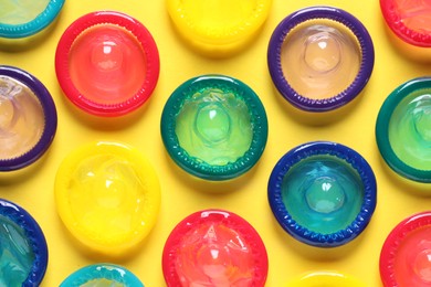 Photo of Colorful condoms on yellow background, flat lay