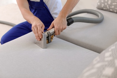 Photo of Dry cleaning worker removing dirt from sofa indoors