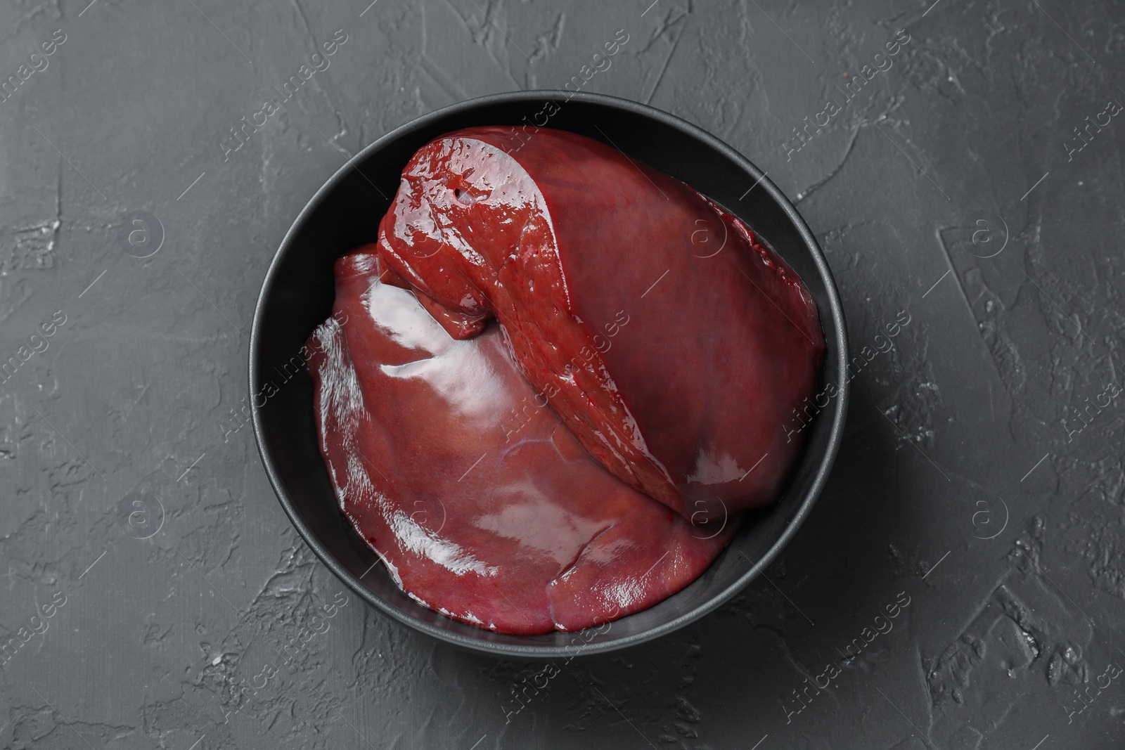 Photo of Pieces of raw beef liver in bowl on black table, top view