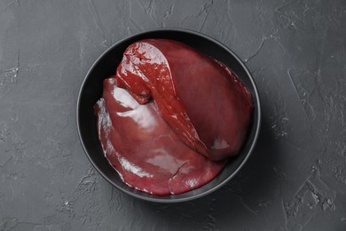 Pieces of raw beef liver in bowl on black table, top view
