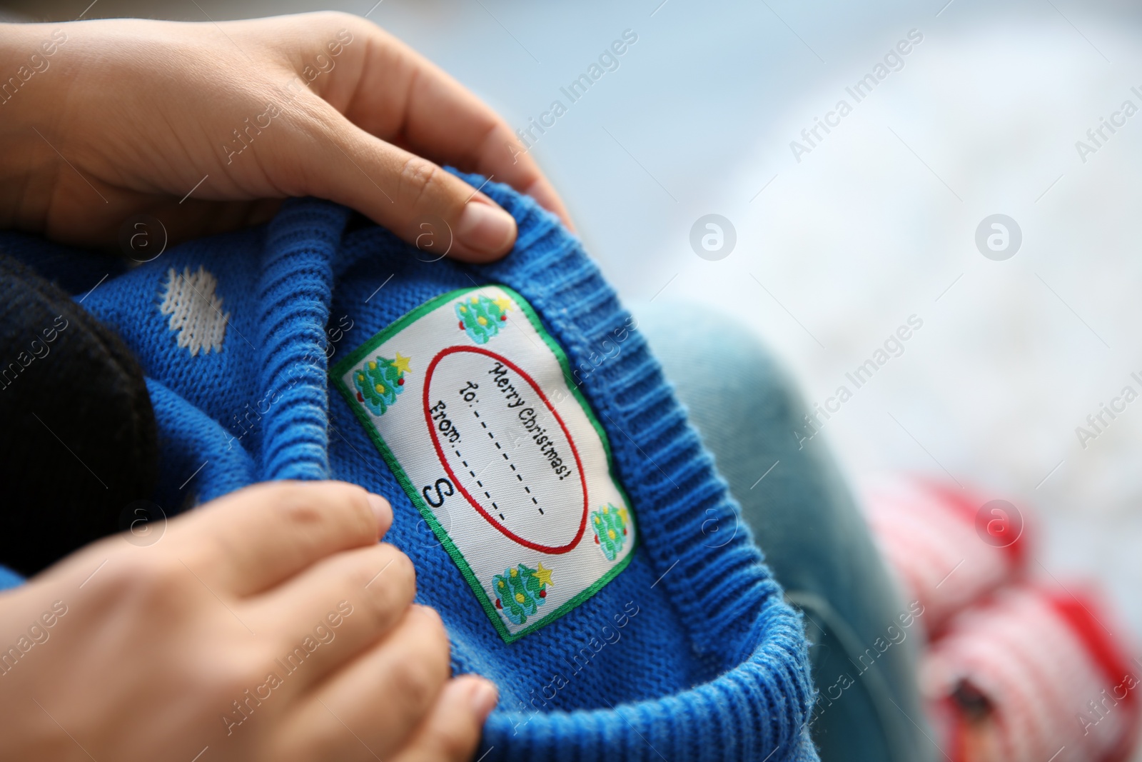 Photo of Woman holding Christmas sweater with tag, closeup