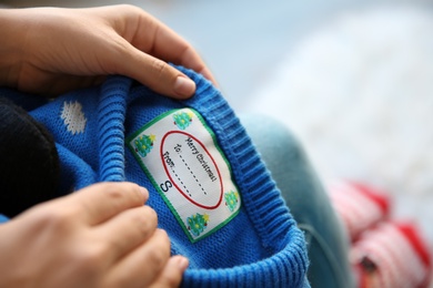 Photo of Woman holding Christmas sweater with tag, closeup