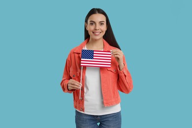 Happy young woman with flag of United States of America on light blue background