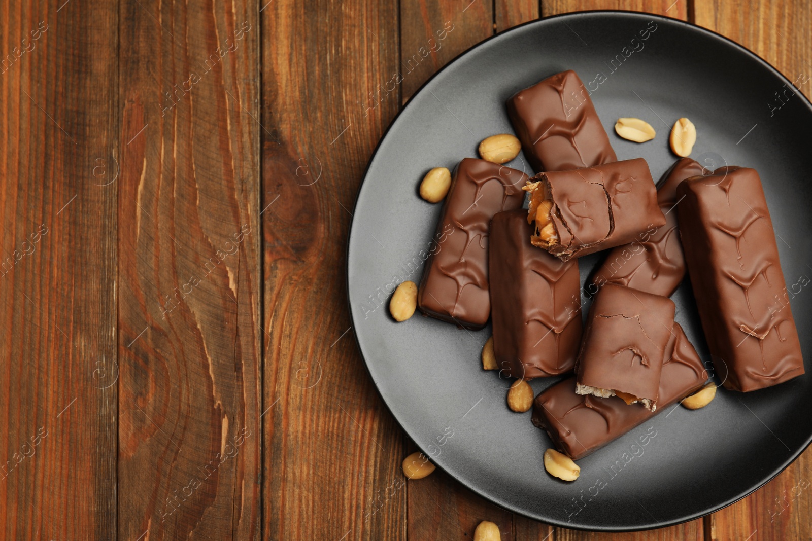 Photo of Plate of chocolate bars with caramel, nuts and nougat on wooden table, top view. Space for text