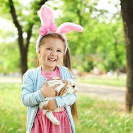 Photo of Little girl with adorable bunny outdoors on sunny day. Easter celebration