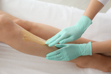 Photo of Woman getting wax epilation of legs in salon, closeup