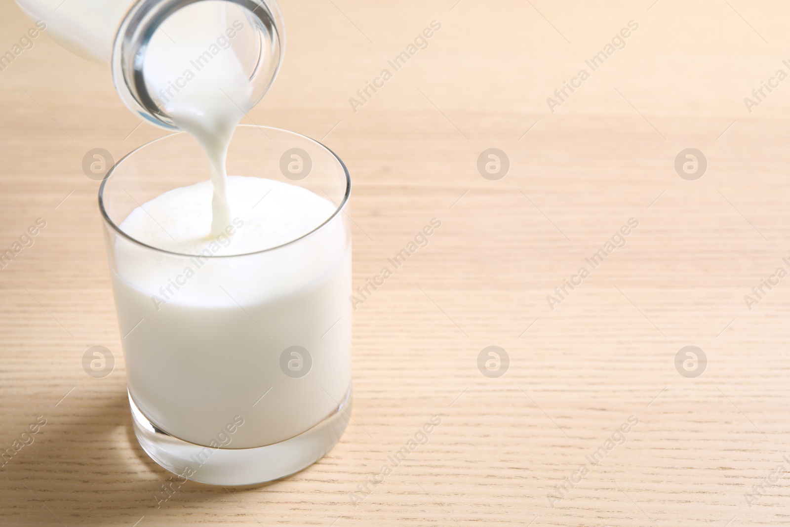 Photo of Pouring milk into glass on wooden table. Space for text