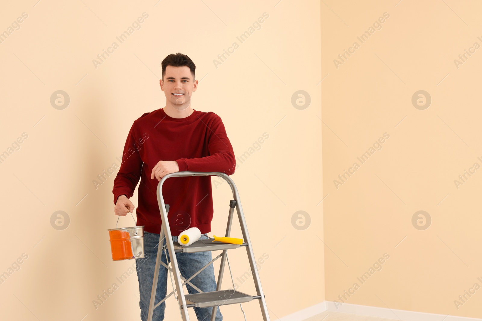 Photo of Young handsome man with paint can near metal stepladder indoors, space for text. Room renovation