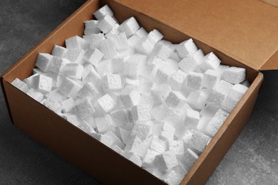 Photo of Cardboard box filled with polystyrene styrofoam pieces on grey table, closeup