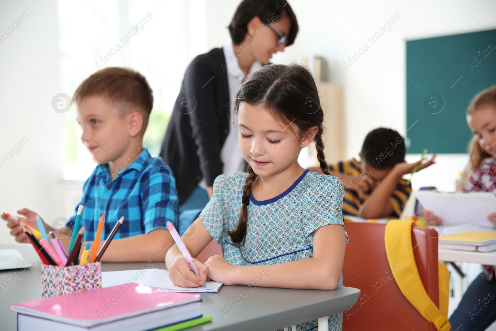 Photo of Adorable little children sitting at desks in classroom. Elementary school