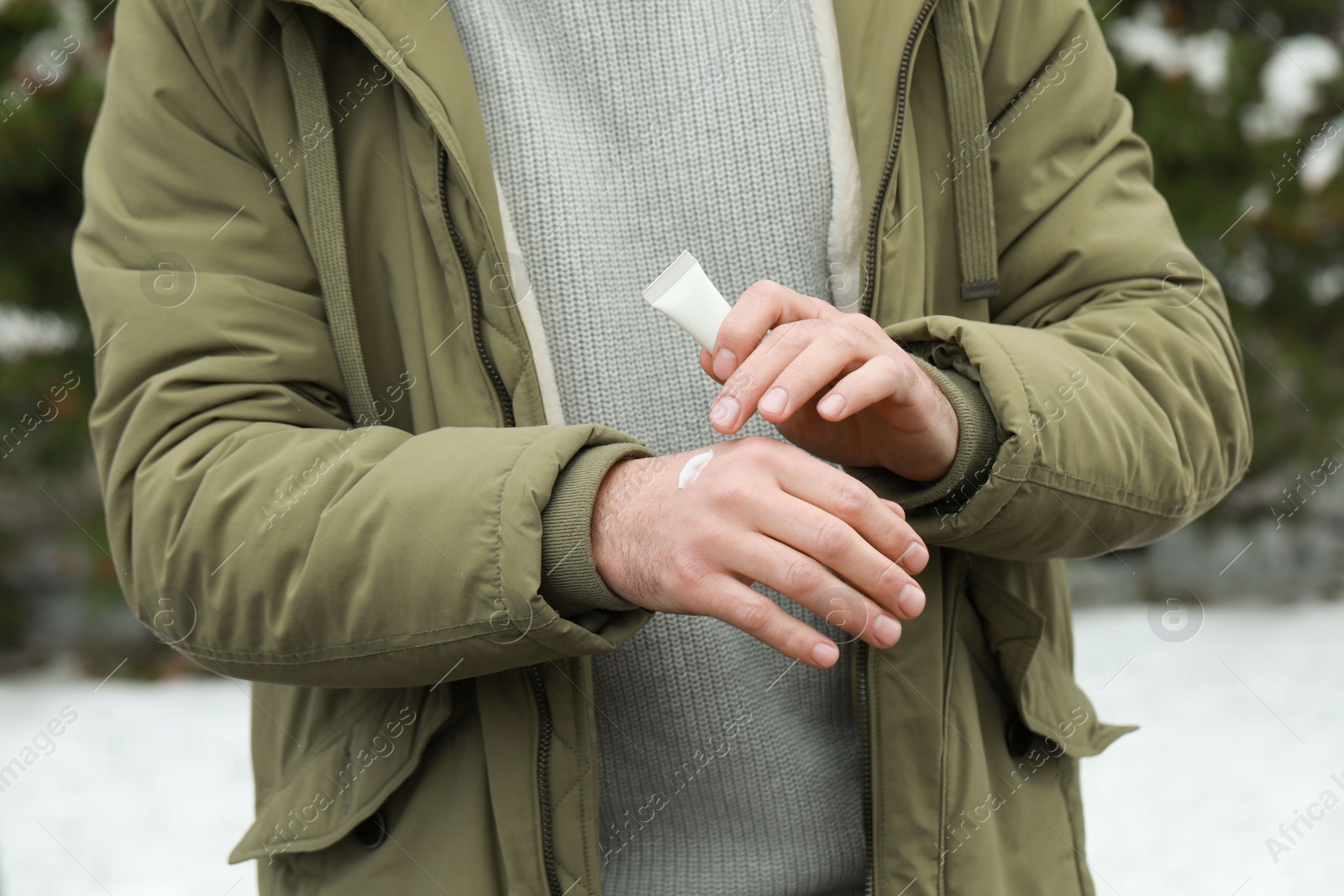 Photo of Man applying cream from tube onto hand outdoors, closeup. Winter care