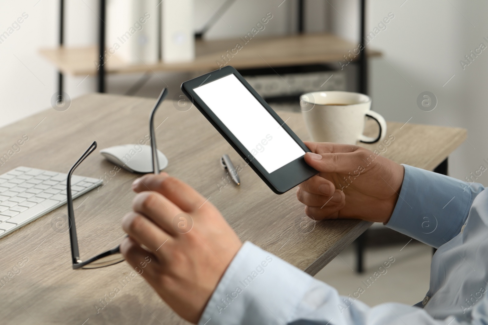 Photo of Man using e-book reader at wooden table indoors, closeup