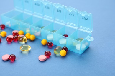 Plastic box with different pills on light blue background, closeup