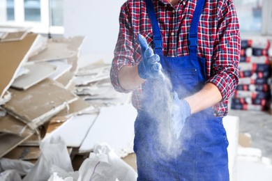 Photo of Construction worker shaking off dust from hands in room prepared for renovation, closeup