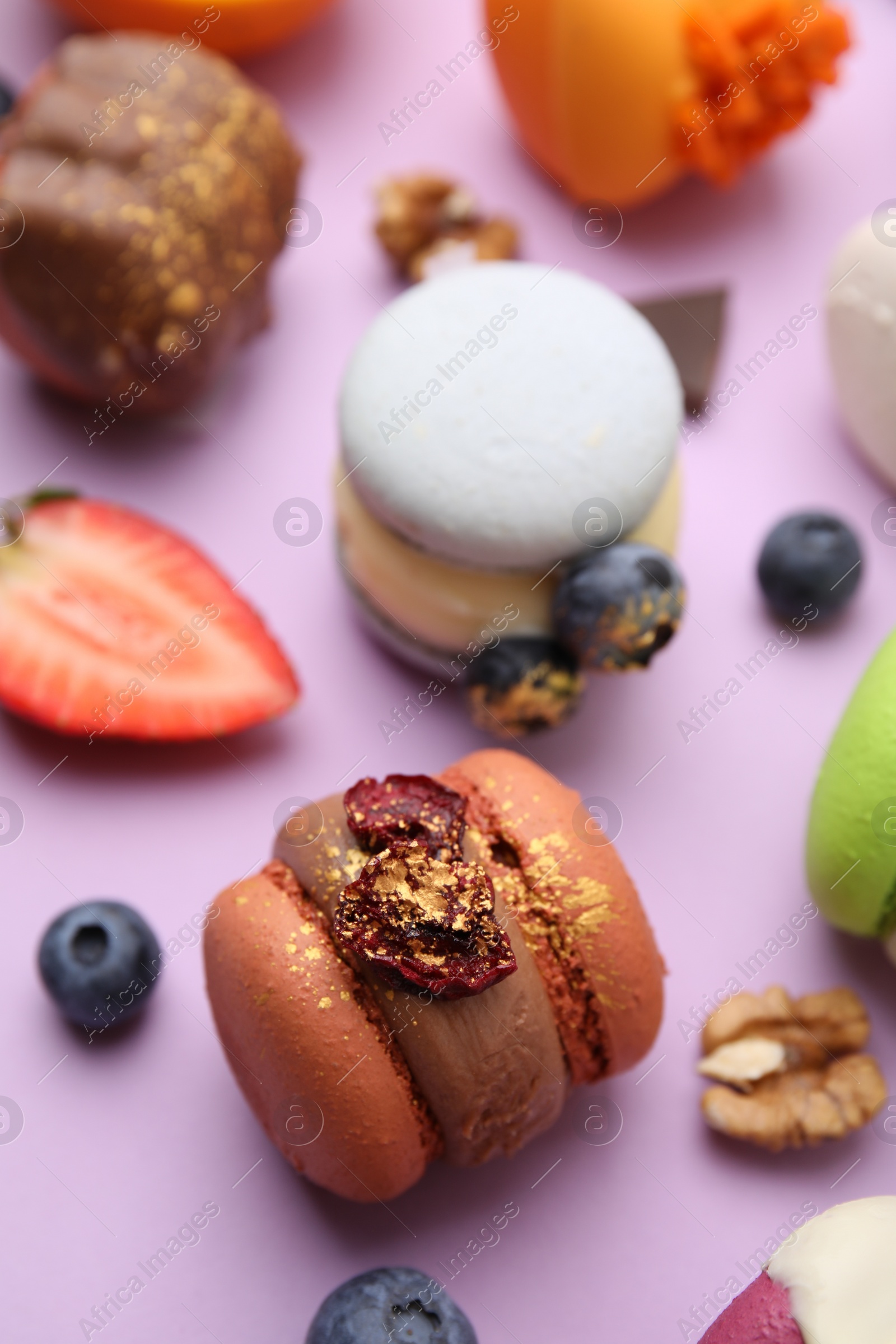 Photo of Delicious macarons and berries on violet table, closeup