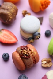 Delicious macarons and berries on violet table, closeup
