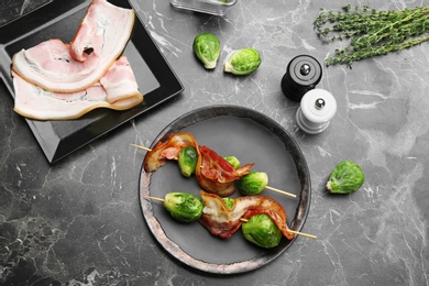 Skewers with Brussels sprouts and bacon served on marble table, flat lay