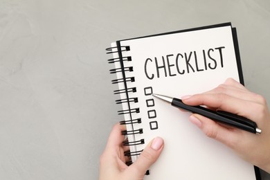Woman filling Checklist at light grey table, top view. Space for text