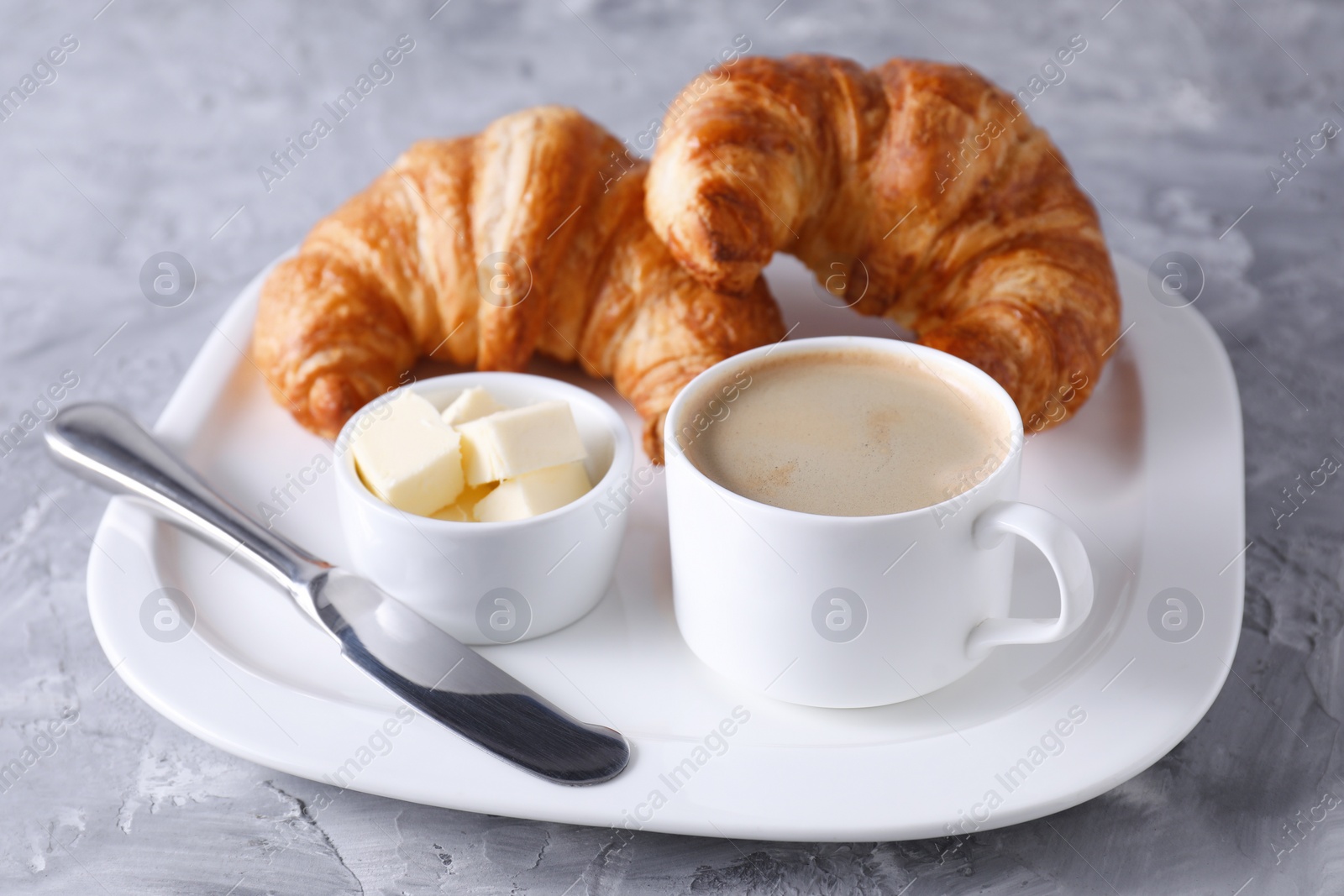 Photo of Tasty breakfast. Cup of coffee, fresh croissants, knife and butter on grey table, closeup