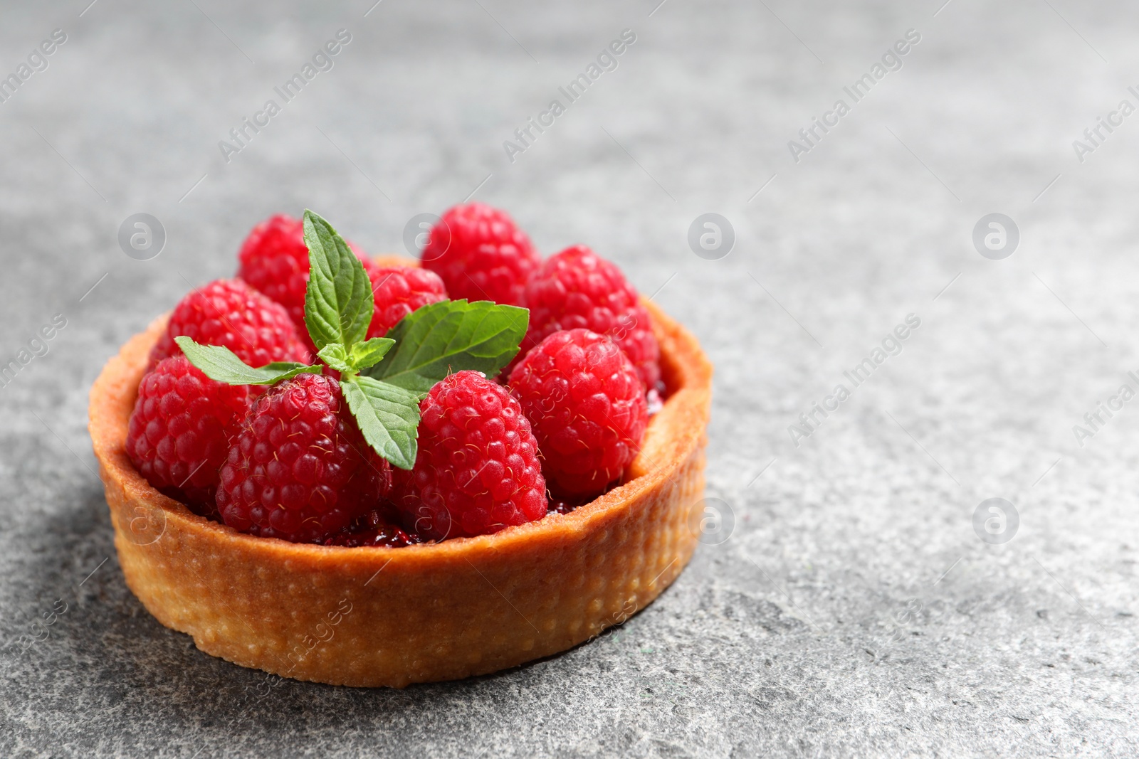 Photo of Tartlet with fresh raspberries on light grey background, closeup and space for text. Delicious dessert