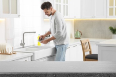 Image of Man doing washing up in kitchen, focus on empty grey stone table