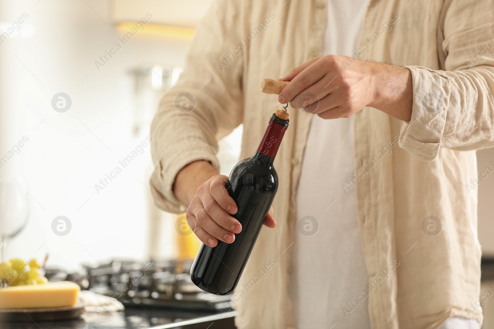 Photo of Man opening wine bottle with corkscrew indoors, closeup. Space for text