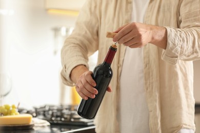 Man opening wine bottle with corkscrew indoors, closeup. Space for text