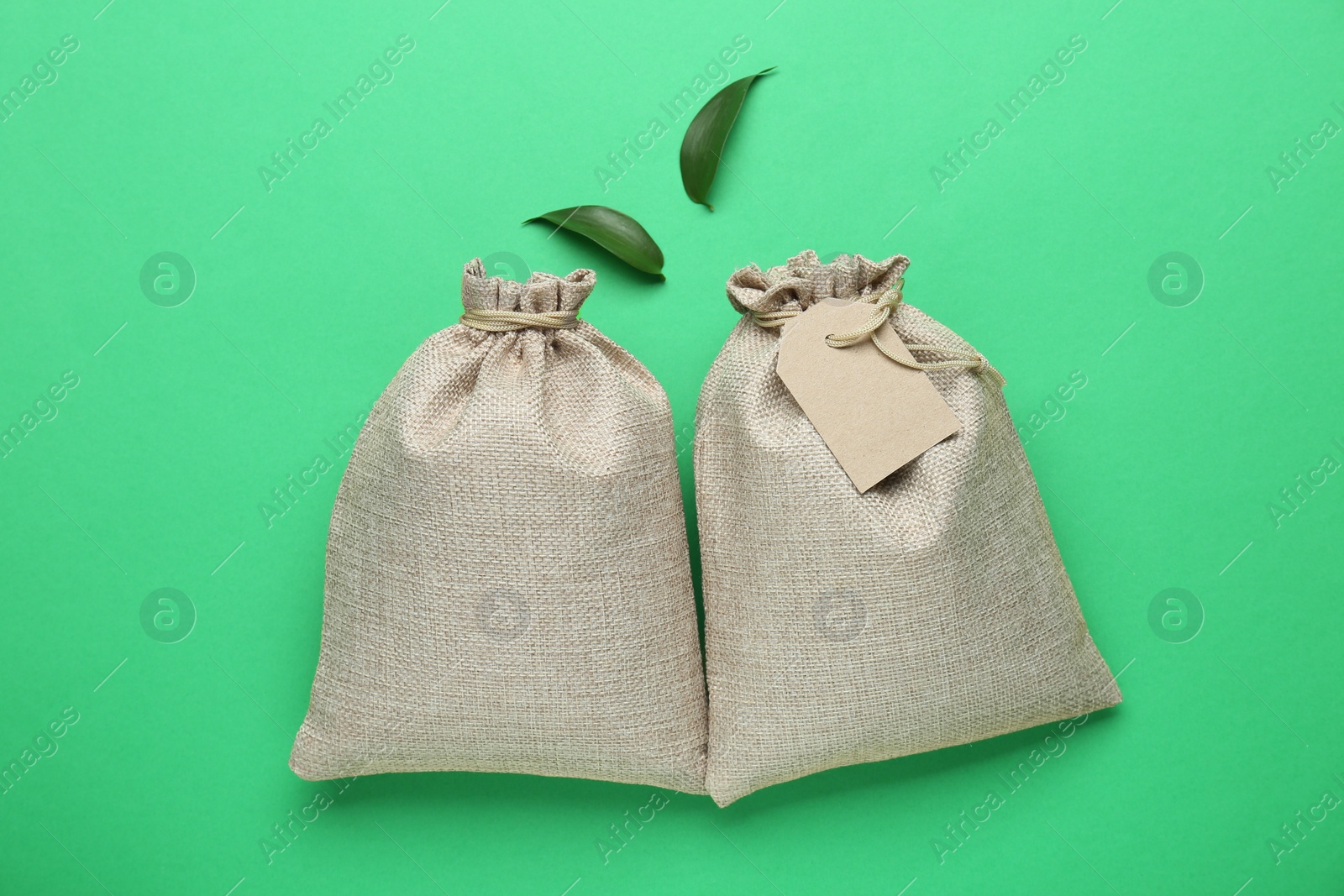 Photo of Tied burlap bags and leaves on green background, flat lay