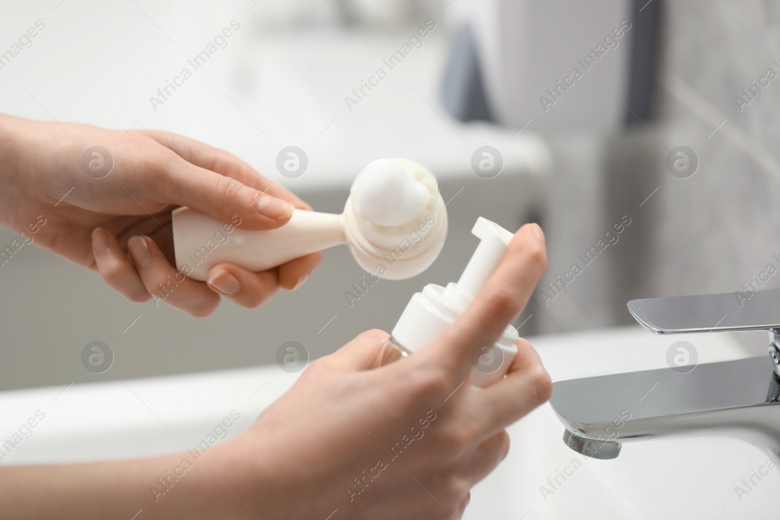 Photo of Washing face. Woman applying cleansing foam onto brush above sink in bathroom, closeup