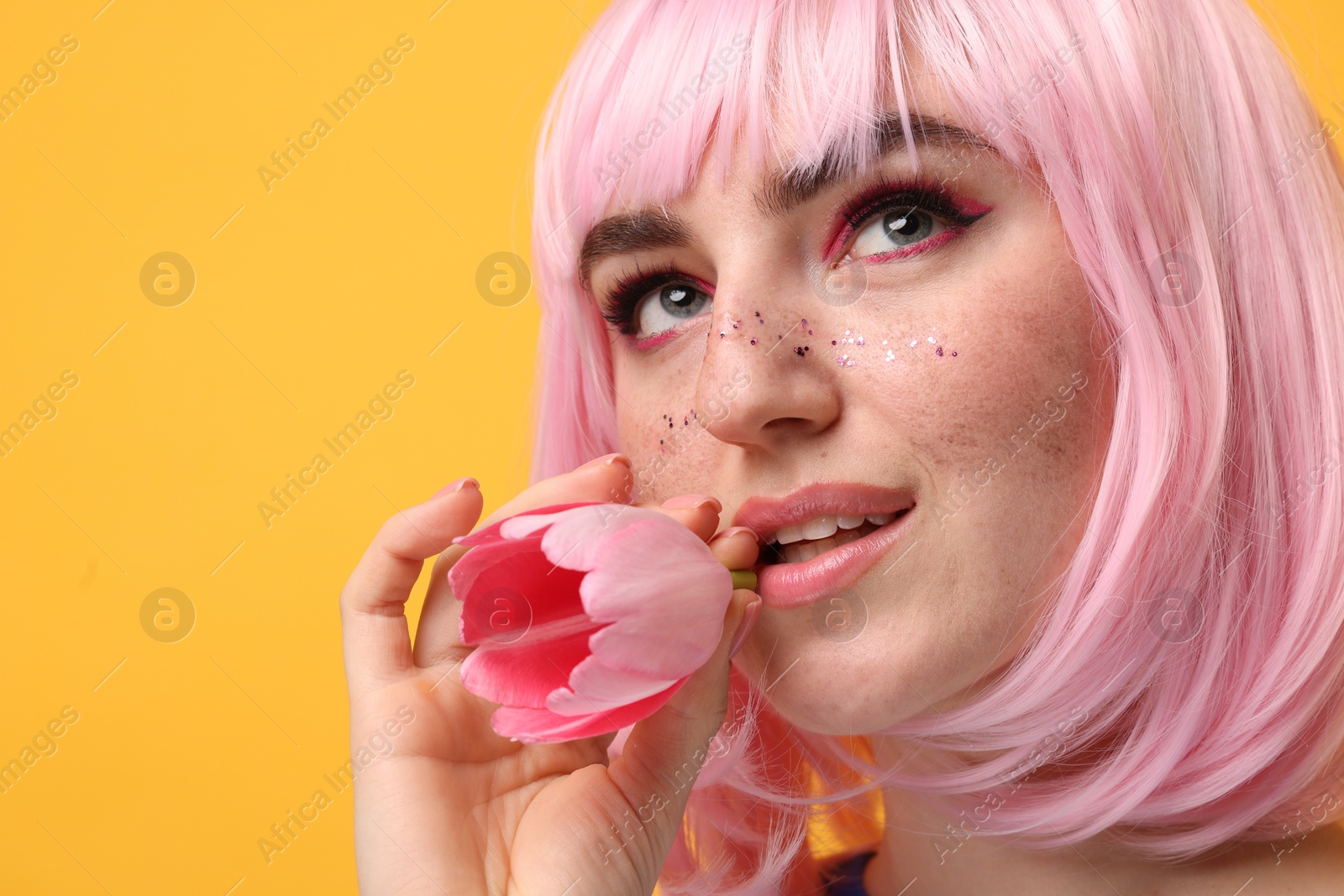 Photo of Beautiful woman with bright makeup and glitter freckles holding tulip on yellow background, closeup. Space for text