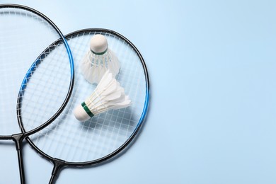 Feather badminton shuttlecocks and rackets on light blue background, top view. Space for text