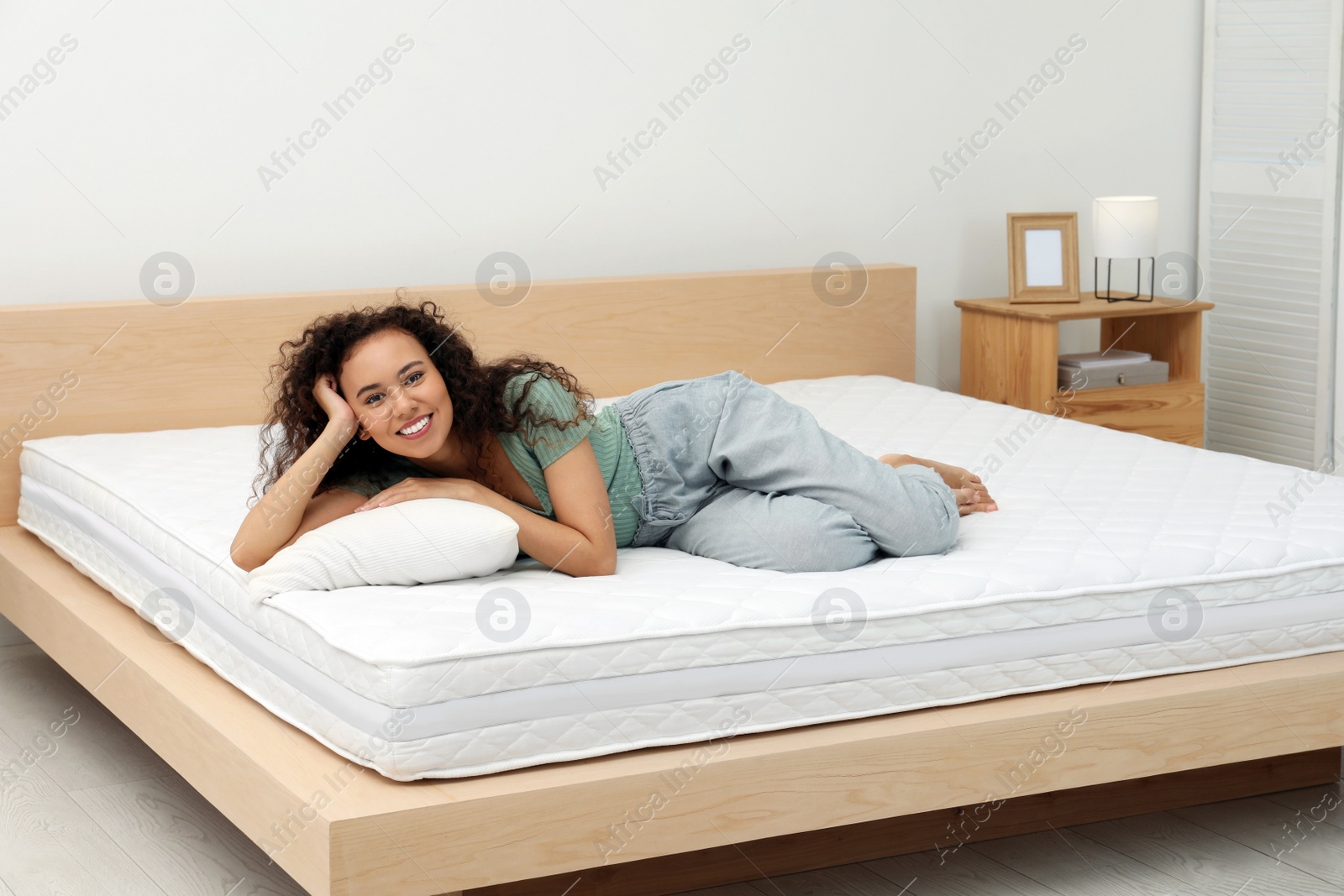 Photo of Happy young African American woman on bed with comfortable mattress and pillow at home