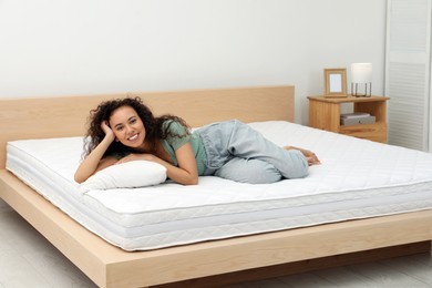 Happy young African American woman on bed with comfortable mattress and pillow at home