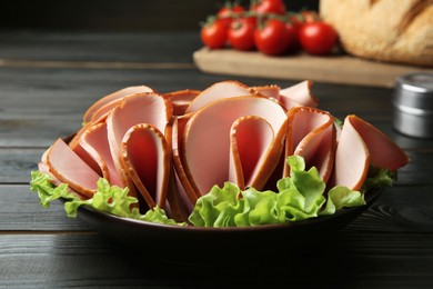 Slices of delicious boiled sausage with lettuce on dark wooden table, closeup