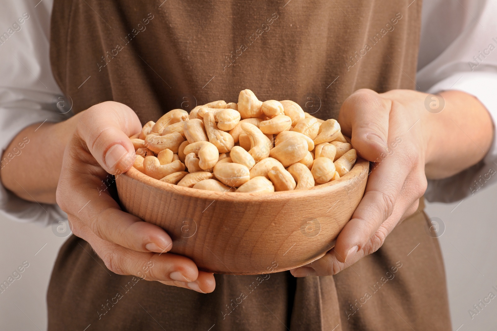 Photo of Woman holding bowl of cashew nuts on light background, closeup