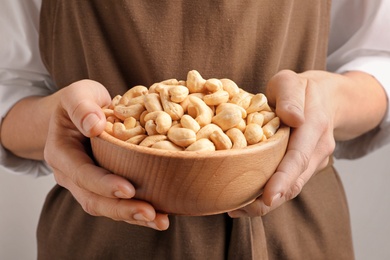 Woman holding bowl of cashew nuts on light background, closeup