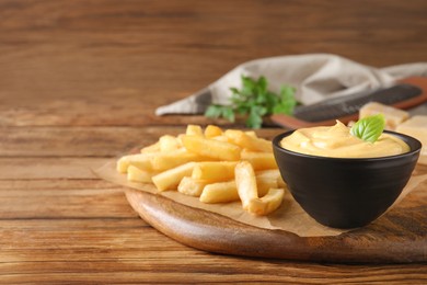 Photo of Delicious French fries and cheese sauce with basil on wooden table, space for text
