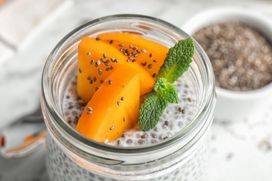 Photo of Jar of tasty chia seed pudding with persimmon on table, closeup