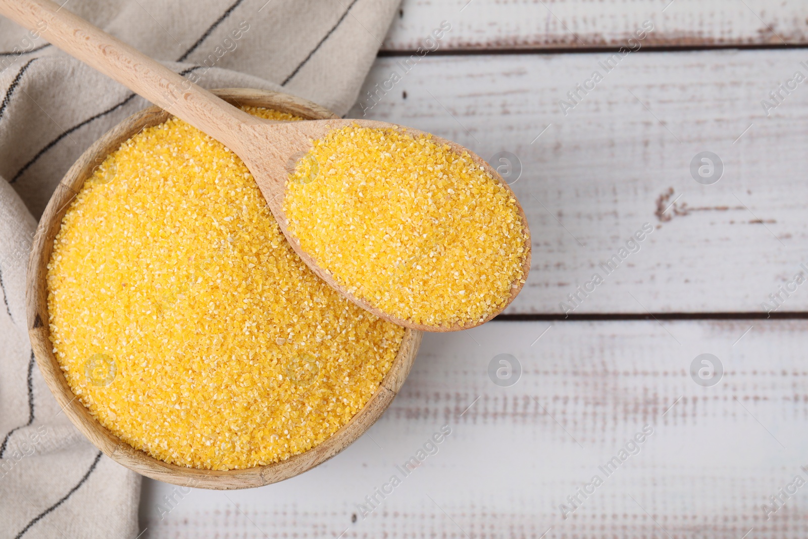 Photo of Raw cornmeal in bowl and spoon on light wooden table, top view. Space for text