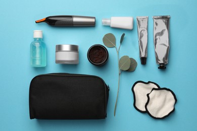 Photo of Preparation for spa. Compact toiletry bag and different cosmetic products on light blue background, flat lay