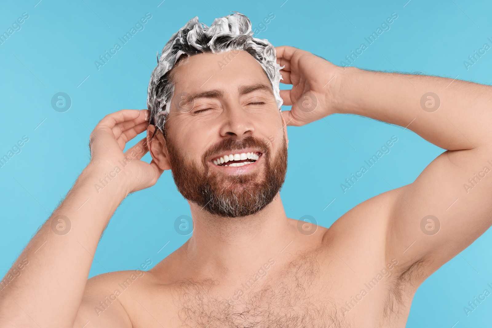 Photo of Happy man washing his hair with shampoo on light blue background