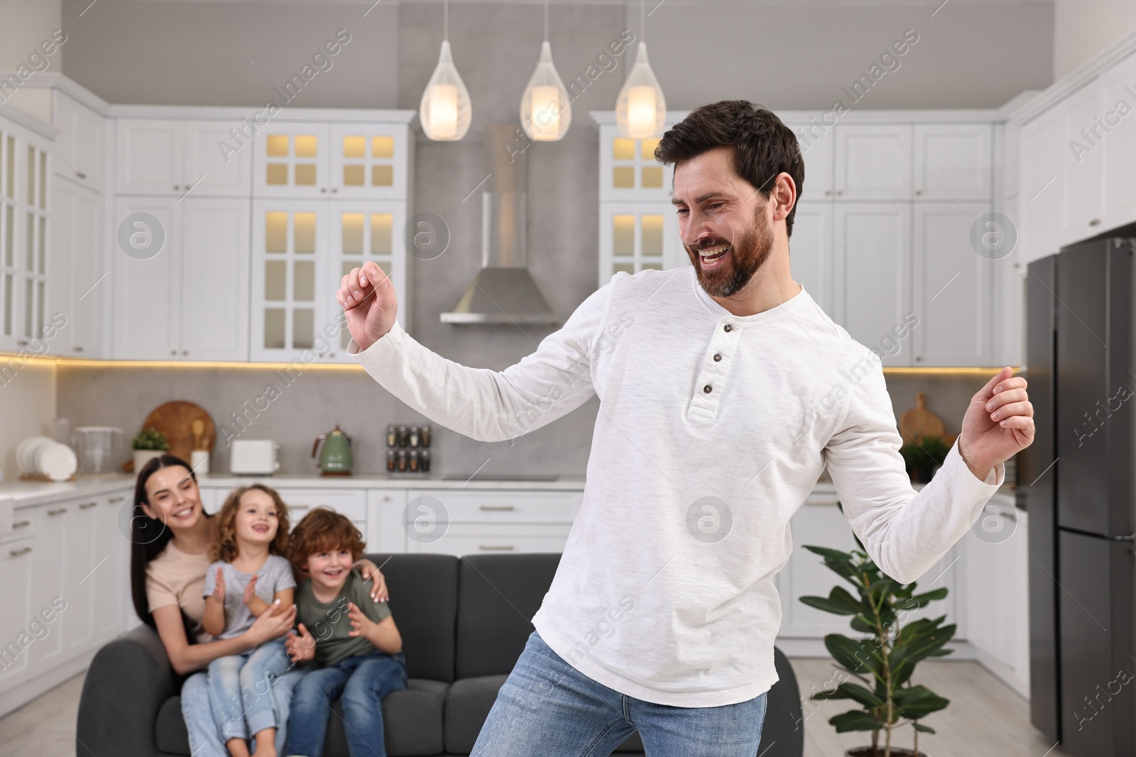 Photo of Happy family having fun at home. Father dancing while his relatives resting on sofa