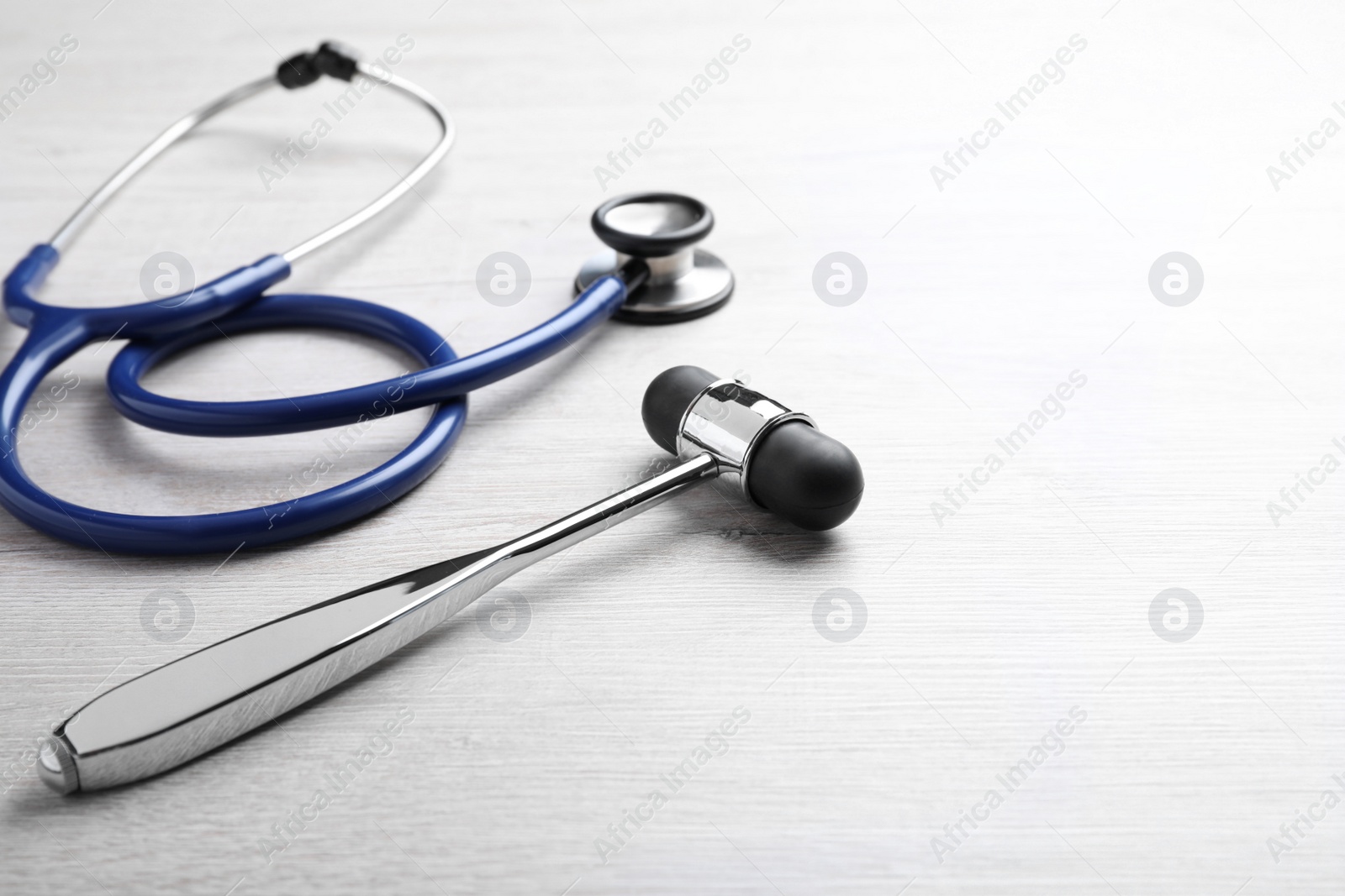 Photo of Reflex hammer with stethoscope on light wooden background, closeup. Nervous system diagnostic